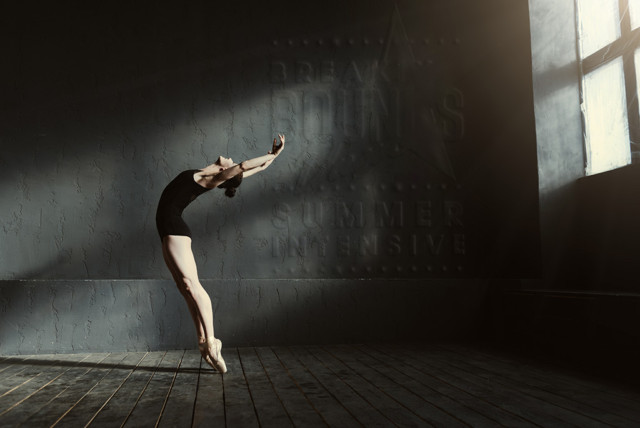 Female dancer arching her back while on her toes in a dark studio